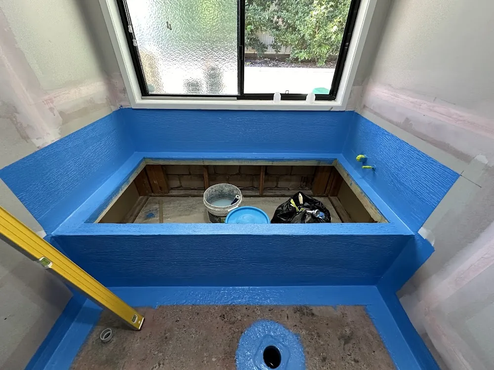 A bath hob and bathroom floor under a window coated in blue waterproofing membrane