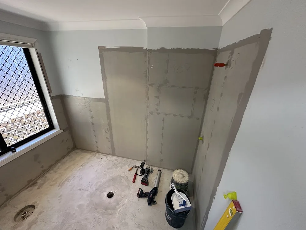 Bathroom walls sheeted and set, with tools on a bare concrete floor, ready for waterproofing