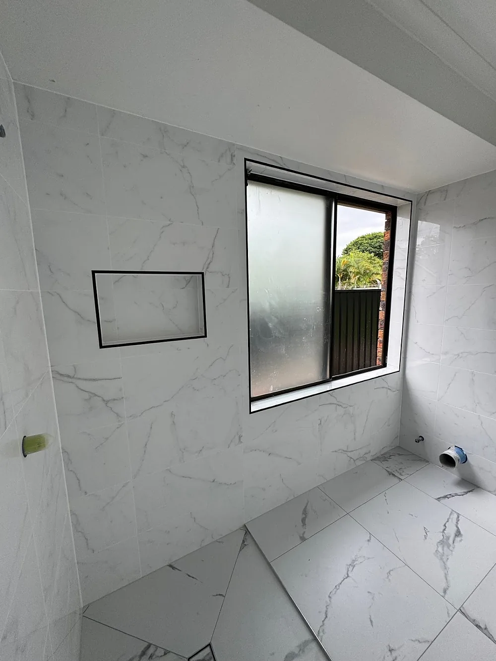 Marble-look wall and floor tiles in a shower with black trim framing the niche and window reveal