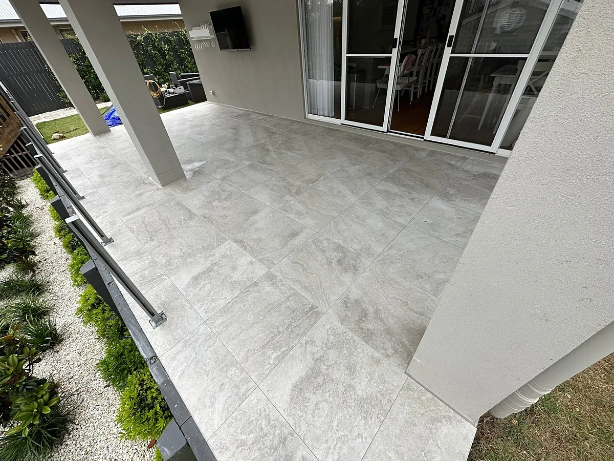 A covered alfresco area tiled in large pale stone-look outdoor tiles beside a garden