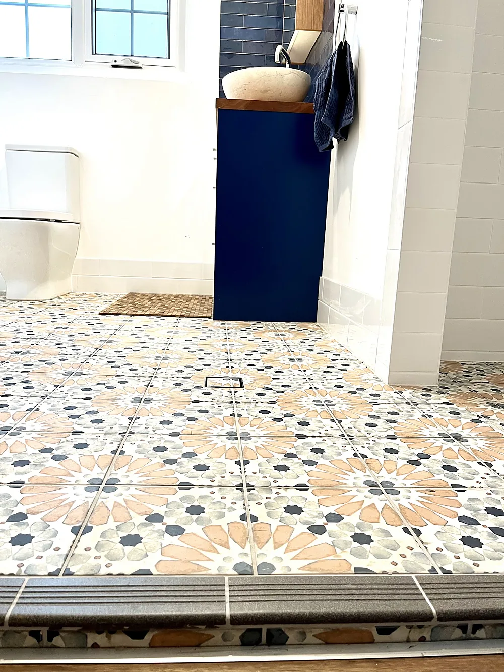 Patterned encaustic-style floor tiles in a bathroom with a navy vanity and a tiled step edge