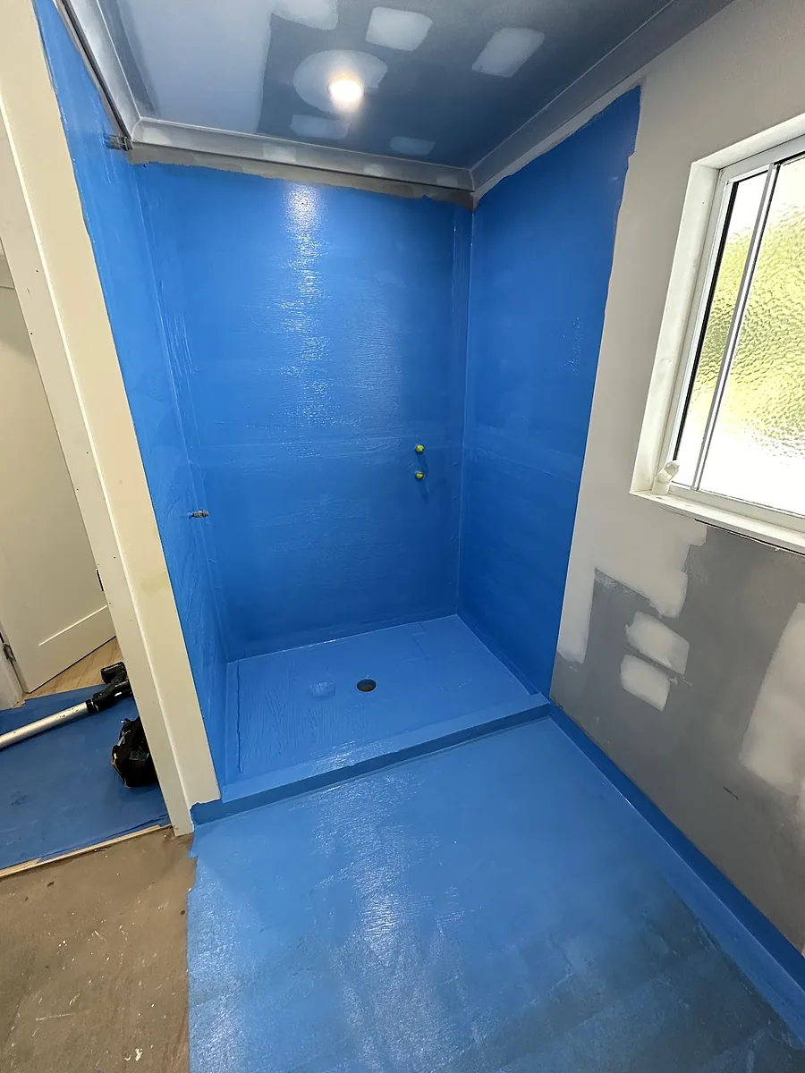 A shower recess and bathroom floor coated in blue waterproofing membrane before tiling
